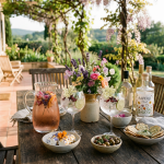 Outdoor table with floral drinks, snacks, flowers, and aperitif bottles